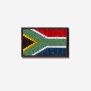 May include: A rectangular embroidered patch featuring the South African flag. The design includes a black triangle on the left, a yellow Y-shape, and horizontal bands of red, white, green, and blue, all enclosed within a dark brown border.