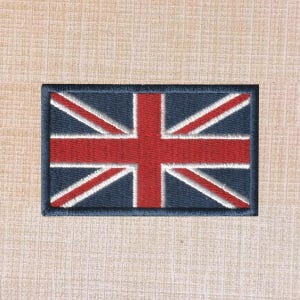 Puede incluir: Un parche rectangular bordado con el diseño de la bandera Union Jack. El parche muestra un fondo azul oscuro con una cruz roja central y franjas diagonales rojas, todo delineado con bordes blancos finos y un borde cosido en azul oscuro.