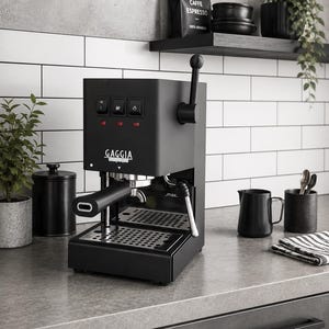 Puede incluir: Una cafetera espresso Gaggia en color negro mate con una palanca vertical en el lado derecho, tres botones de control cuadrados con luces indicadoras rojas, un portafiltros con mango negro, una bandeja de goteo de acero inoxidable y vaporizador.
