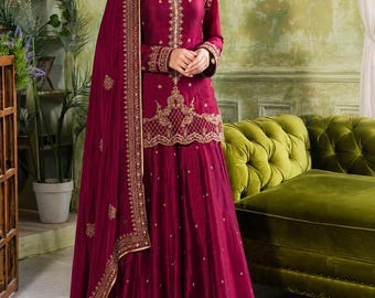 Peut inclure: Un ensemble composé d'une tunique à manches longues et d'une jupe longue de couleur magenta profond, orné de broderies dorées complexes sur l'encolure, l'ourlet et les poignets. Il comprend un dupatta magenta transparent à bordure dorée.
