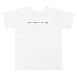 May include: White toddler t-shirt with the phrase "please don't tell me about blippi." printed in black, centered on the front. The shirt has short sleeves and a crew neck.