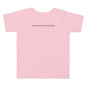 May include: A light pink toddler t-shirt with the text "please don't tell me about blippi." printed in black. The shirt has short sleeves and a crew neck. The t-shirt is made of a soft material.