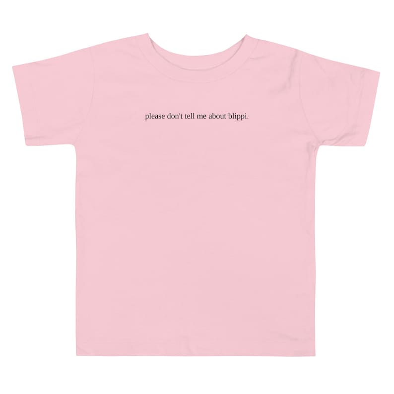 May include: A light pink toddler t-shirt with the text "please don't tell me about blippi." printed in black. The shirt has short sleeves and a crew neck. The t-shirt is made of a soft material.