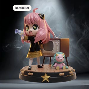 以下が含まれることがあります： ピンクの髪、黒と金のドレス、おもちゃの銃を持ったキャラクターのフィギュア。フィギュアは、ヴィンテージテレビとピンクのぬいぐるみのある木製のステージに立っています。ベースは黒で、金の星とピーナッツ型のディテールがあります。「Bestseller」という言葉が白いバブルに入っています。