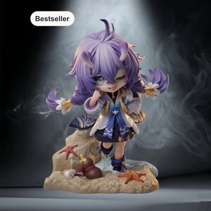 以下が含まれることがあります： 紫色の髪と遊び心のある表情をしたキャラクターのフィギュア。青と白のアクセントが施された詳細な衣装を着ています。フィギュアは、ヒトデと小さなひょうたんのある砂浜のベースの上に立っています。「Bestseller」という言葉が左上にあります。