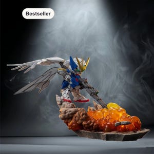Könnte beinhalten: Detaillierte Actionfigur eines Roboters mit weißen Flügeln, blau-weißer Rüstung und einem goldenen Helm, der eine Waffe hält. Die Figur steht auf einem felsigen Sockel mit orangefarbenen und gelben Flammen. Das Wort "Bestseller" steht in einem weißen Oval.