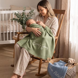 Può includere: Una coperta per neonati in maglia verde salvia con il nome Everly James ricamato in corsivo bianco, e una coperta blu con il nome Ethan Patrick ricamato in bianco, entrambe caratterizzate da un motivo a maglia waffle testurizzato.