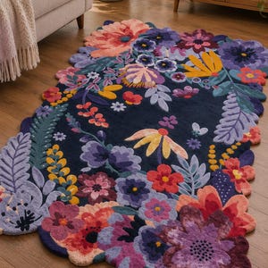 May include: A rectangular area rug with a dark navy blue background featuring a dense, colorful floral pattern. The rug has an irregular, scalloped edge that follows the contours of the various flowers in shades of pink, purple, yellow, and teal.