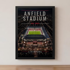Könnte beinhalten: Ein gerahmter Druck des Anfield Stadium, der Heimat des FC Liverpool, bei Nacht. Das Bild zeigt das beleuchtete Spielfeld und die Tribünen des Stadions mit dem Text "ANFIELD STADIUM" und "LIVERPOOL" in Weiß.