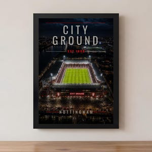 May include: A framed print of City Ground, Nottingham, a soccer stadium at night. The image shows the stadium's illuminated field and stands, with the text "CITY GROUND" and "EST. 1898" at the top. The word "NOTTINGHAM" is at the bottom.
