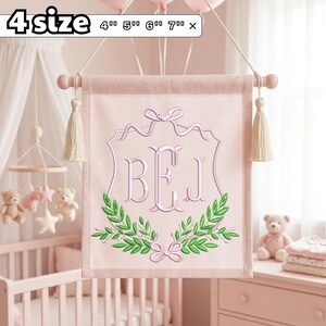 Op de afbeelding: Een lichtroze stoffen wandbanner met het geborduurde monogram BEJ in een decoratief schildframe met groene laurierbladeren en een roze strik. De banner hangt aan een houten roede met crèmekleurige kwastjes en de tekst 4 size 4" 5" 6" 7".