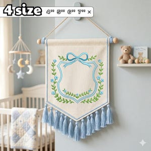 May include: A beige fabric wall banner featuring an embroidered blue shield outline, a light blue bow at the top, and green vine accents with small blue flowers. The banner has light blue tassels along the bottom edge and text reading 4 size 4" 5" 6" 7".