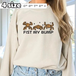 May include: A beige crewneck sweatshirt featuring a graphic of three brown crabs and the text FIST MY BUMP. The design includes small black stars. A size chart overlay indicates available sizes of 4 inches, 5 inches, 7 inches, and 9 inches.