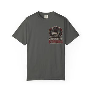 May include: A charcoal gray t-shirt featuring a graphic design for Iowa Volunteer Strong. The design includes a firefighter's Maltese cross emblem with the state name and the words "Volunteer Strong" in red and white.