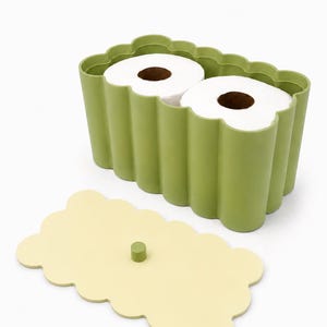 May include: A sage green rectangular storage container with a scalloped edge design, holding two rolls of white toilet paper. The container includes a separate, flat, pale yellow lid with a small, centered sage green cylindrical knob handle.