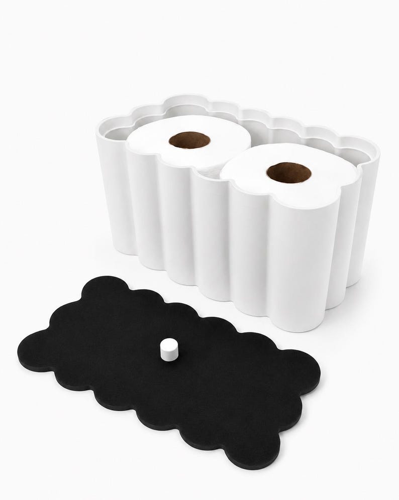 May include: A white, scalloped-edge rectangular container holding two rolls of white toilet paper, accompanied by a separate black, scalloped-edge lid featuring a small, centered white cylindrical knob for easy removal and placement.