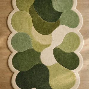 Könnte beinhalten: Ein Teppich mit unregelmäßigem, gewelltem Rand und getufteter Oberfläche. Das Design besteht aus überlappenden, abgerundeten organischen Formen in verschiedenen Schattierungen von Waldgrün, Olivgrün, Salbeigrün und Creme, eingefasst von einer cremefarbenen Bordüre.