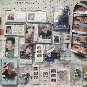 May include: A collection of K-pop merchandise featuring various photo cards, cassette tapes, and pins with portraits of young individuals. The items include text labels like Juhoon, Martin, and Cortis, displayed on a white surface with black dots.