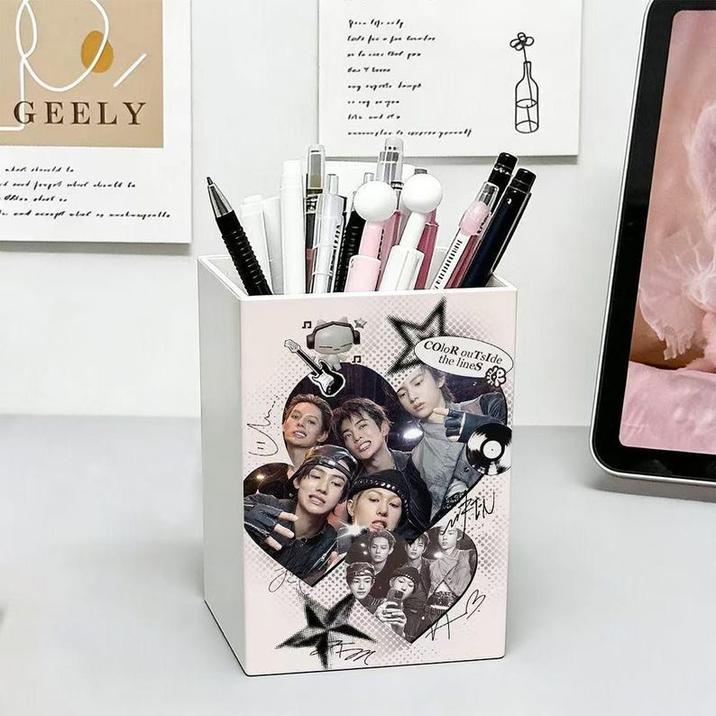 May include: A white rectangular desk organizer filled with various pens and markers. The front features a collage of black and white portraits of young people, a guitar graphic, stars, and the text "COLOR outSide the lineS" in a circular badge.