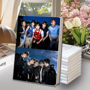 May include: A rectangular notebook featuring a two-part photographic cover. The top section shows five individuals in casual clothing against a dark blue background. The bottom section displays four individuals in black jackets against a blue sky.