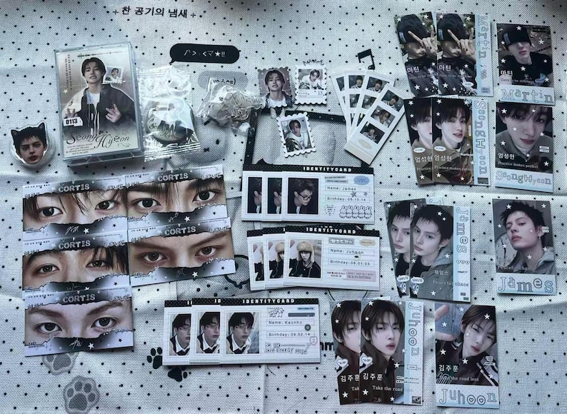 May include: A collection of K-pop merchandise including a cassette case, identity cards, photo strips, and individual portrait cards featuring various individuals. The items are decorated with star motifs and text labels like Cortis, James, and Juhoon.