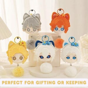 May include: Five plush character head keychains with animal ears, each featuring a metal ring, a small flower accessory, and a fluffy pom-pom. The characters have distinct hair colors including gray, orange, yellow, white with blue, and white with blue.