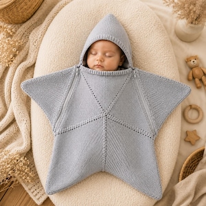 Puede incluir: Una manta de arrullo tejida en color gris claro con forma de estrella, capucha puntiaguda y dos cremalleras diagonales que van desde el cuello hasta las puntas laterales. La prenda presenta un patrón de punto texturizado con costuras visibles.