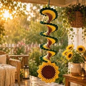May include: A hanging crochet spiral decoration featuring a repeating pattern of dark green, yellow, and brown yarn. The spiral structure terminates in a large, circular sunflower motif with a dark brown center and bright yellow petals.