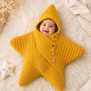 May include: A mustard yellow crocheted baby swaddle blanket shaped like a five-pointed star with a pointed hood. The garment features a diagonal front closure secured by two round brown buttons and two small wooden star-shaped buttons.