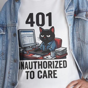 Puede incluir: Una camiseta blanca con un gráfico de un gato negro sentado en un escritorio con un ordenador, una pila de papeles y una taza. El texto sobre el gato dice 401 y el texto debajo dice UNAUTHORIZED TO CARE. La camiseta se lleva bajo una chaqueta vaquera.