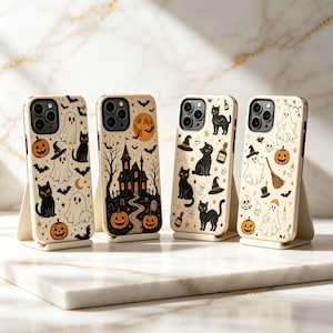 May include: Four smartphone cases featuring Halloween-themed illustrations. The designs include black cats, ghosts, pumpkins, a haunted house, bats, and witch hats in a color palette of black, orange, and cream, displayed on individual stands.
