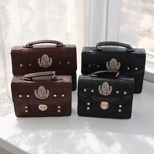 May include: Four structured satchel bags in dark brown and black, each featuring a top handle, a front flap with a metallic push-lock closure, decorative straps with gold-tone studs, and an embroidered crest emblem on the center front.