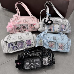 Könnte beinhalten: Fünf rechteckige Handtaschen in Pink, Silber, Weiß, Hellblau und Schwarz. Jede Tasche hat eine durchsichtige Vordertasche mit Anime-Charakter-Prints, sternförmigen Metallbeschlägen, silbernen Ketten und Plüsch-Anhängern an den Trägern.