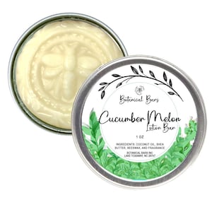May include: A round tin container with a white label that reads "Botanical Bars Cucumber Melon Lotion Bar 1 OZ INGREDIENTS: COCONUT OIL, SHEA BUTTER, BEESWAX, AND FRAGRANCE BOTANICAL BARS INC LAKE TOXAWAY, NC 28747". The label has a green leafy design. The tin is open and shows a white lotion bar inside.