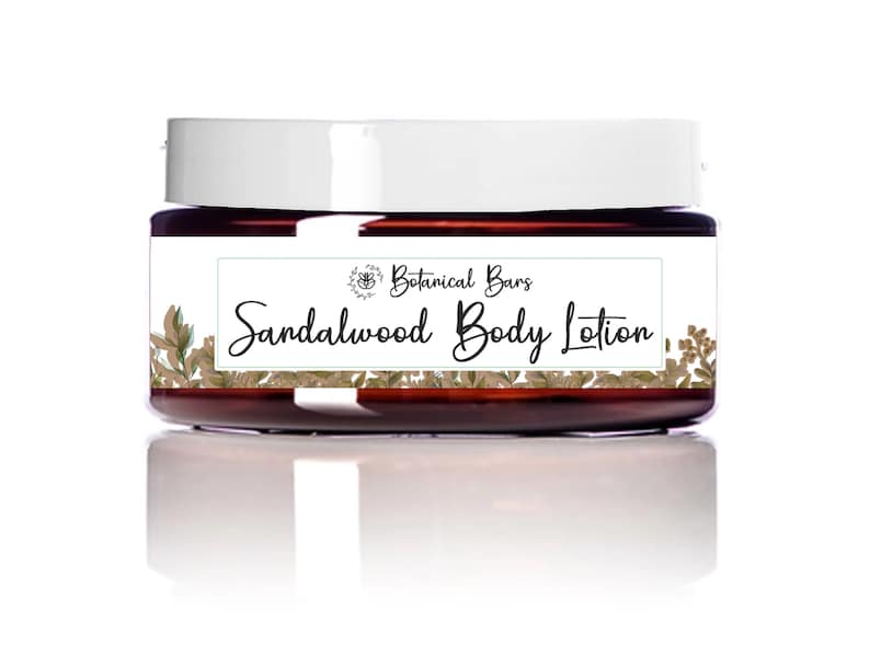 May include: A jar of sandalwood body lotion from Botanical Bars. The jar is a dark amber color with a white lid. The label features the text "Sandalwood Body Lotion" in a script font, with botanical illustrations.