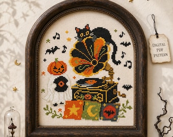 May include: A cross-stitch pattern in a dark wood arched frame featuring a black cat perched on a vintage gramophone, a ghost with a pumpkin head, musical notes, and stars. A tag attached to the frame reads Digital PDF Pattern in black text.