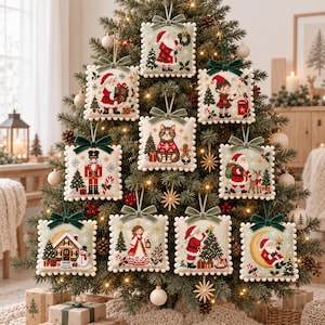 May include: A collection of ten square, cross-stitched Christmas ornaments hanging on a pine tree. Each ornament features a unique holiday design, including Santa Claus, an elf, a nutcracker, a cat, an angel, and a gingerbread house, all finished with a velvet ribbon.
