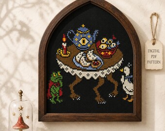 May include: A cross-stitch pattern in a dark wood arched frame featuring a table with clawed legs, a blue teapot with an eye, a candle, and food. A green frog in a red cape and a white duck stand nearby. A tag reads DIGITAL PDF PATTERN.