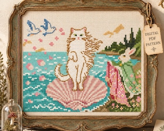 May include: A cross-stitch embroidery in a decorative frame featuring a white cat standing on a pink seashell in blue water, with two blue birds above and a white rabbit in a green cloak on the shore. A tag reads DIGITAL PDF PATTERN.