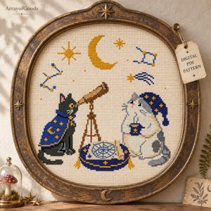 May include: A cross-stitch embroidery in a round, distressed bronze frame featuring a black cat in a blue star-patterned cape looking through a telescope, and a grey cat in a matching nightcap holding a mug, with celestial motifs and a digital PDF pattern tag.