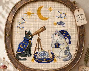 May include: A cross-stitch embroidery in a round, distressed bronze frame featuring a black cat in a blue star-patterned cape looking through a telescope, and a gray cat in a matching nightcap holding a mug, with celestial motifs and a digital PDF pattern tag.
