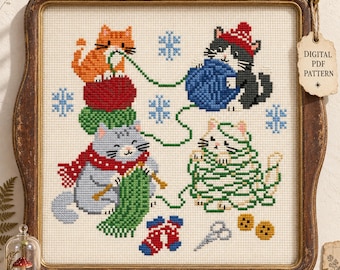May include: A cross-stitch pattern featuring four cats playing with yarn, including an orange cat, a gray cat with a red scarf, a black cat in a red hat, and a white cat tangled in green yarn, with blue snowflakes, scissors, and buttons.