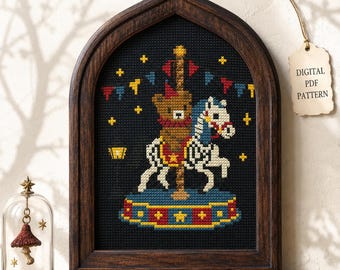 May include: A cross-stitch pattern in a dark wooden arched frame featuring a brown bear riding a white carousel horse on a blue and red platform. The background is black with yellow stars and colorful triangular bunting flags. A tag reads DIGITAL PDF PATTERN.