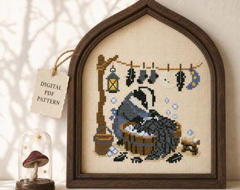 May include: A cross-stitch pattern featuring a badger washing laundry in a wooden tub, with clothes hanging on a line, a lantern, and a moon. A tag reads "DIGITAL PDF PATTERN" and "ArrayofGoods". A small mushroom is displayed under a glass dome.