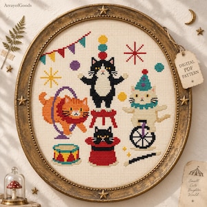 May include: A cross-stitch embroidery in an oval frame featuring a circus theme with cats. The design includes a black and white cat on a stool, an orange cat jumping through a hoop, a white cat on a unicycle, a cat in a top hat, and a drum.