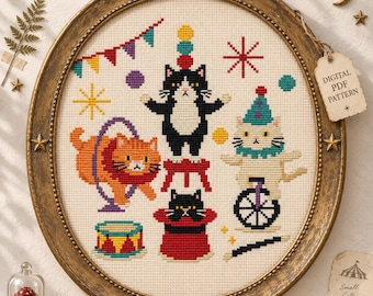 May include: A cross-stitch embroidery in an oval frame featuring a circus theme with cats. The design includes a black and white cat on a stool, an orange cat jumping through a hoop, a white cat on a unicycle, a cat in a top hat, and a drum.