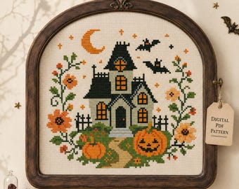 May include: A cross-stitch pattern featuring a haunted house, a crescent moon, bats, and pumpkins framed in a dark wood arch. The design includes orange flowers and green vines on a cream fabric. A tag attached to the frame reads Digital PDF Pattern.