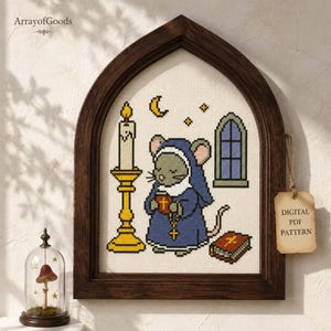 Puede incluir: Un patrón de punto de cruz en un marco de madera oscura con forma de arco que muestra un ratón gris con hábito azul, sosteniendo un libro y un rosario. Junto al ratón hay una vela amarilla en un soporte, un libro y una ventana. Etiqueta: DIGITAL PDF PATTERN.