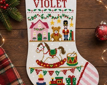 May include: A white Christmas stocking featuring cross-stitch embroidery with the name VIOLET at the top. The design includes a pink house, a brown teddy bear, a nutcracker, a rocking horse, a drum, a toy train, and colorful holiday bunting.