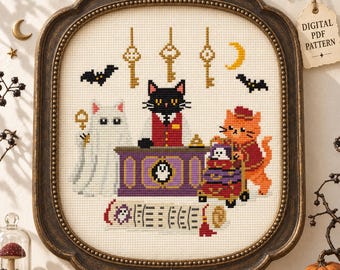 May include: A cross-stitch pattern featuring a black cat in a red vest behind a purple desk, an orange cat with a luggage cart, and a white ghost. The design includes hanging gold keys, bats, a crescent moon, and a scroll, all framed in dark wood.